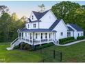 Elegant white farmhouse with a spacious covered porch, rocking chairs, and meticulously maintained landscaping at 1023 Laura Johnson Rd, Pittsboro, NC 27312