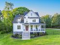 Inviting white farmhouse featuring a covered porch with seating, complemented by lush landscaping and a green lawn at 1023 Laura Johnson Rd, Pittsboro, NC 27312