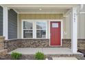 Welcoming covered front porch with brick base, neat shrubs and a striking red front door at 3705 Rosebush Dr, Zebulon, NC 27597