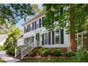 Two-story white home featuring black shutters, a brick chimney, and lush landscaping with stairs to the front door at 1002 Springmill Ct, Apex, NC 27502
