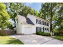 Side view of a charming white home with black shutters, lush landscaping, attached garage, and a concrete driveway at 1002 Springmill Ct, Apex, NC 27502