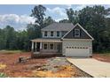 New two-story home featuring gray siding, a two-car garage and a covered front porch in a wooded area at 5516 Jaeger Dr # 75, Graham, NC 27253