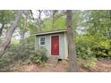 Small shed with a red door and window, nestled among trees and greenery, providing extra storage space at 7312 Ray Rd, Raleigh, NC 27613