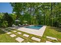 Backyard swimming pool surrounded by stone tile and green grass with lounge chairs under shaded umbrellas at 3312 Rock Creek Dr, Raleigh, NC 27609