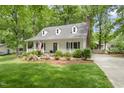 Charming home with a covered front porch, dormer windows, lush landscaping, and a brick chimney on the side at 404 Trappers Run Dr, Cary, NC 27513
