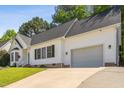 Side view of white home featuring an attached garage with a concrete driveway and manicured lawn at 8401 Hobhouse Cir, Raleigh, NC 27615