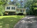 Two-story home with yellow siding, brick foundation, covered front porch, lush greenery, and a long driveway at 7412 Barberry Ct, Raleigh, NC 27615