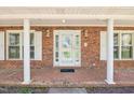 Covered front porch with brick flooring, white columns and a glass front door at 3011 Old Hillsborough Rd, Mebane, NC 27302