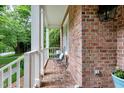Cozy covered front porch with brick flooring, white pillars, and comfortable seating, framed by lush greenery at 5112 Wolcott Ct, Fuquay Varina, NC 27526