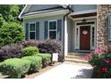 Front entrance featuring a charming doorway framed by stone accents, lush landscaping, and blooming flowers at 1108 Kalworth Rd, Wake Forest, NC 27587