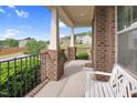 Wide shot of a relaxing covered front porch with iron railing, brick pillars, and a white bench at 5004 Clowser Minnow Ct, Wake Forest, NC 27587
