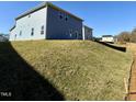 The backyard features a newly built home with blue siding on a grassy hill under a bright blue sky at 1667 Pecan Drive # 25, Nashville, NC 27856