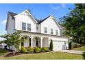 Bright home featuring a large two-car garage, a front porch with rocking chairs, and mature landscaping at 128 Highland Grove Way, Fuquay Varina, NC 27526