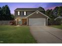 Home exterior at dusk features a teal front door, a garage and well-kept lawn at 401 Onondaga Ct, Holly Springs, NC 27540