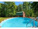 Inviting in-ground pool with views of a log cabin guest house surrounded by lush green trees at 515 Tramway West Rd, Sanford, NC 27330
