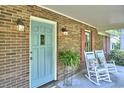 Close-up of a charming brick home's blue front door, flanked by rocking chairs and potted plants at 5319 Memory Ln, Durham, NC 27712