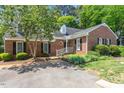 A cozy one-story brick home featuring black shutters, complemented by lush landscaping and a verdant tree at 1623 Village Glenn Dr, Raleigh, NC 27612