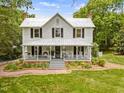 Inviting two-story farmhouse with a spacious front porch, mature trees, and a brick walkway at 967 Bynum Rd, Pittsboro, NC 27312