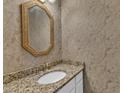 Elegant powder room features a granite countertop, oval sink, gold-framed mirror, and patterned wallpaper at 11944 Appaloosa E, Raleigh, NC 27613
