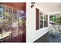 Inviting front porch detail with glass door, white railing, rocking chair, and window with red shutter at 5414 Stanley Rd, Durham, NC 27704