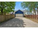 Detached blue garage with a concrete driveway and a white door is surrounded by a wooden fence and lush green trees at 420 Marsh Landing Dr, Holly Springs, NC 27540