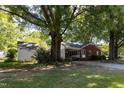 Exterior view of a brick home, a covered carport and a white storage shed surrounded by mature trees at 210 S Hughes St, Apex, NC 27502