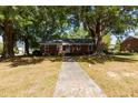 Quaint brick home featuring mature trees, green lawn and a walkway leading to the front door at 210 S Hughes St, Apex, NC 27502