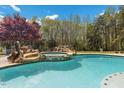 Outdoor swimming pool with integrated hot tub surrounded by natural rock formations and greenery at 6707 Frieden Church Rd, Gibsonville, NC 27249
