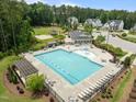 Aerial view of a community pool with lounge chairs, tables, and a clubhouse in a wooded neighborhood on a sunny day at 3700 Horton Hill Dr, New Hill, NC 27562