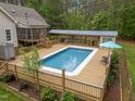 Aerial view of a rectangular pool with a wooden deck, covered seating area, and a lush green tree line at 3653 Range Rd, Stem, NC 27581