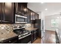 Modern kitchen with dark cabinetry, stainless steel appliances, granite countertops, and stylish backsplash at 1101 Boxcar Way, Apex, NC 27502