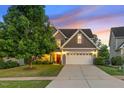 Beautiful home at dusk, featuring a manicured lawn, stone accents, and a two-car garage at 117 Woodlark Ln, Holly Springs, NC 27540
