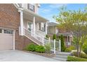 Inviting home entrance featuring a covered porch, white railings, brick accents, and landscaped garden at 844 Cozy Oak Ave, Cary, NC 27519