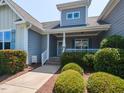 Inviting front porch with decorative shrubs, columns, and a sign that says 