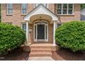 Close-up of a charming brick front porch with columns, a black door, and neatly trimmed bushes at 108 Nimbus Ct, Cary, NC 27513