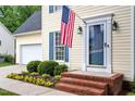 Close-up view of the home's front porch showcasing a blue door, an American flag, and brick steps at 1614 Finnsbury Dr, Burlington, NC 27217