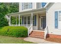 Inviting covered front porch with brick steps, white railings, and a view of the landscaped front yard at 6002 Whisperwood Dr, Durham, NC 27713