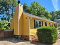 Side view of yellow house featuring chimney, well-kept landscaping and brick foundation at 3612 Satellite Ct, Raleigh, NC 27604
