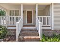 Inviting front porch with brick steps, white railings, columns, and a stained wood front door at 316 Waterford Dr, Clayton, NC 27520
