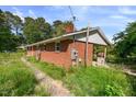 Side view of a brick home showing a covered area and utility features, surrounded by a natural landscape at 995 Shawtown Rd, Lillington, NC 27546