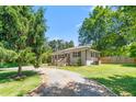 View of a charming brick home featuring manicured bushes, a wooden fence, and gravel driveway at 827 Loop Rd Rd, Burlington, NC 27217