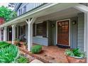 Covered front porch featuring classic columns, brick flooring, a wooden front door, and a cozy seating area at 1513 Dellwood Dr, Raleigh, NC 27607