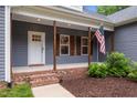 Inviting front porch with brick steps, American flag, and wooden pillars, creating a warm welcome at 1850 Willie Pace Rd, Burlington, NC 27217