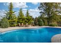 Sparkling blue pool with stone fire pit and Adirondack chairs surrounded by lush landscaping at 8709 Kimalden Ct, Wake Forest, NC 27587