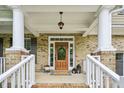 Charming front porch with brick flooring, white columns, and a decorative wooden front door at 1008 Wolfs Bane Dr, Apex, NC 27539