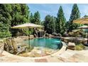 Resort-style pool featuring rock waterfall, mature trees, and stone patio perfect for relaxation at 404 Brightling Way, Holly Springs, NC 27540