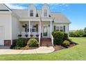 Inviting front porch with brick steps, classic white columns, lush landscaping, and a decorative American flag at 518 Spruce Meadows Ln, Willow Springs, NC 27592