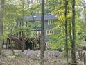 Exterior backyard view of two-story home with a wooden deck and stairs, enveloped by lush greenery and mature trees at 5314 Taproot Ln, Durham, NC 27705