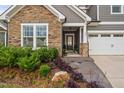 Inviting home exterior with stone accents, a covered porch, a two-car garage, and manicured landscaping at 829 Churton Pl, Cary, NC 27518