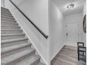A staircase with carpet steps, a dark handrail, and a white wall is adjacent to wood-look flooring at 81 Paperwhite Pl # 213, Clayton, NC 27527